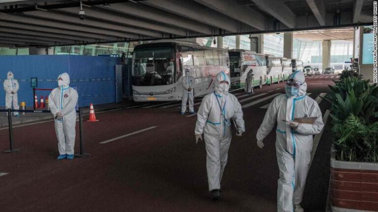 Health workers stand next to buses at a cordoned-off section